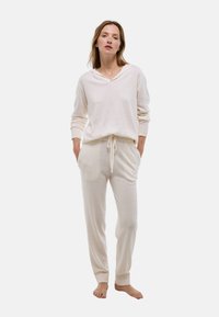 Ensemble de vêtements d'intérieur beige clair comprenant un haut à capuche à manches longues avec poignets côtelés et un pantalon à cordon de serrage avec poches latérales et chevilles côtelées.