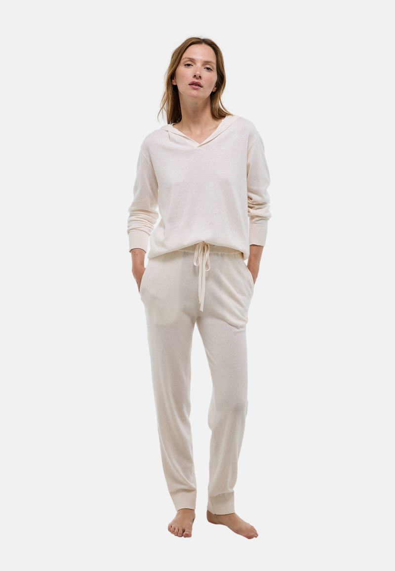 Ensemble de vêtements d'intérieur beige clair comprenant un haut à capuche à manches longues avec poignets côtelés et un pantalon à cordon de serrage avec poches latérales et chevilles côtelées.