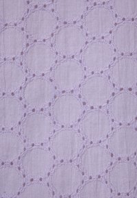 Light purple fabric with a textured pattern featuring embroidered circles connected by floral motifs. The design is intricate and decorative.