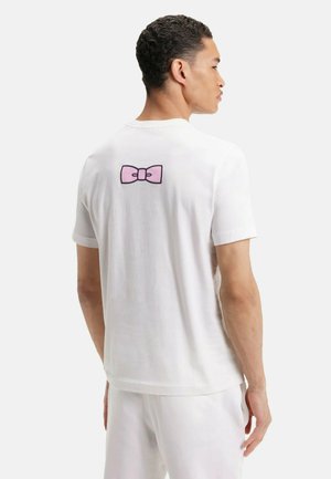 T-shirt en coton blanc avec un motif de nœud rose au centre du dos. Manches courtes et coupe décontractée. Texture lisse.