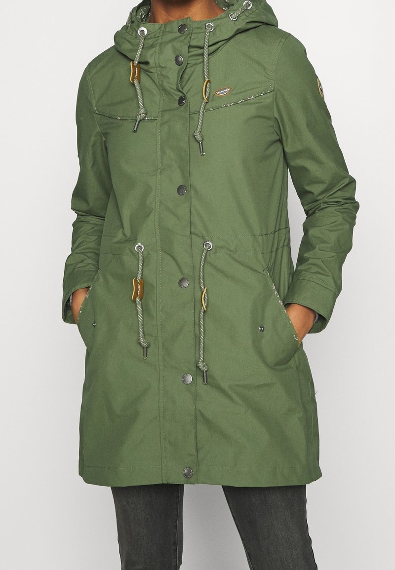 Grön parkajacka i knälängd, tillverkad av vattentåligt material. Har en huva, dragsko, tryckknappar och två framfickor.