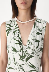 Floral print dress featuring a deep V-neck, light fabric with green leaves on a white background, and a twisted front detail.
