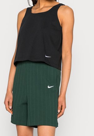 Osoba nosząca czarny bezrękawnik typu crop top i ciemnozielone prążkowane szorty, oba z małymi białymi logo Nike Swoosh.