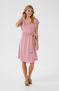 Dusty pink wrap dress with short sleeves, waist tie, and a flared skirt. Smooth fabric and knee-length design. Brown shoes complete the look.
