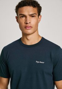 Námornícky modré bavlnené tričko so zaobleným výstrihom a bielym logom "Pepe Jeans" na ľavej hrudi. Hladká textúra, krátke rukávy.