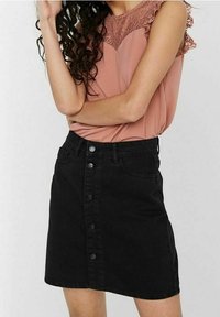 Black denim skirt with front button closure, five pockets, and a fitted shape. Worn with a blush lace-accented top.