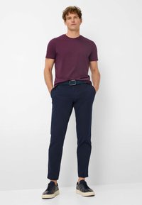 Maglietta corta viola abbinata a pantaloni navy e sneakers nere. La maglietta è liscia; i pantaloni hanno una vestibilità slim con una leggera texture.