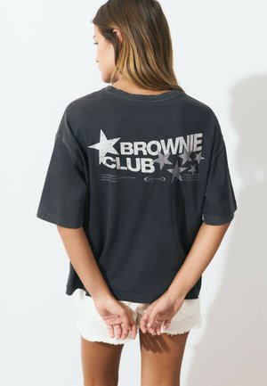 Black oversized T-shirt with "BROWNIE CLUB" in white text and star graphics on the back. Soft texture and relaxed fit. Short sleeves.