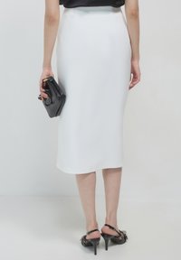 Weiße Bleistiftrock mit glatter Textur, knielang, kombiniert mit schwarzen, eleganten High Heels und einer schwarzen Clutch.