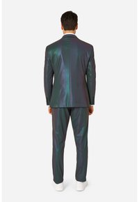 Iridescerend pak met een nauwsluitende pasvorm, bestaande uit een mix van diepe groene en blauwe tinten, een gladde textuur en witte sneakers.