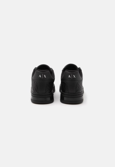 Paire de baskets noires avec panneaux latéraux matelassés vues de dos, avec logos blancs "A|X" sur les talons.