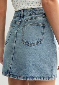 Džínová sukně světle modré barvy s klasick�ým áčkovým střihem, zadními kapsami, viditelným švem uprostřed a detaily třepení na lemu.