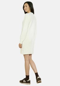 Abito in maglia bianco con motivo a trecce, maniche lunghe e scollatura rotonda, abbinato a sneaker scure e calzini marroni.
