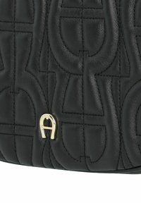 Borsa in pelle nera con un design trapuntato e un accentuato dettaglio oro. La texture è liscia, mostrando un motivo in rilievo.