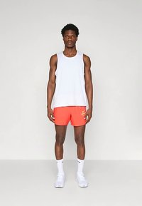 Λευκό αμάνικο τοπ και λαμπερά πορτοκαλί σορτς με την επιγραφή "LONG" σε λευκό χρώμα. Φοριέται με λευκές κάλτσες και αθλητικά παπούτσια, σε ουδέτερο φόντο.