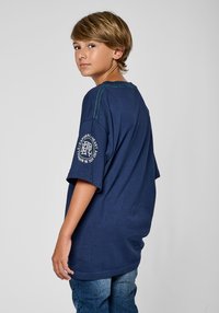 T-shirt en coton bleu marine avec des manches courtes, couture verte le long des épaules et un logo sur la manche gauche. Coupe décontractée.
