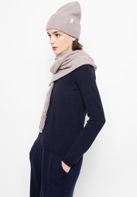 Világosszürke gyapjú sapka és hozzáillő sál egy sötétkék pulóveron, texturált anyagból készült, illeszkedő, lezser kialakítással.