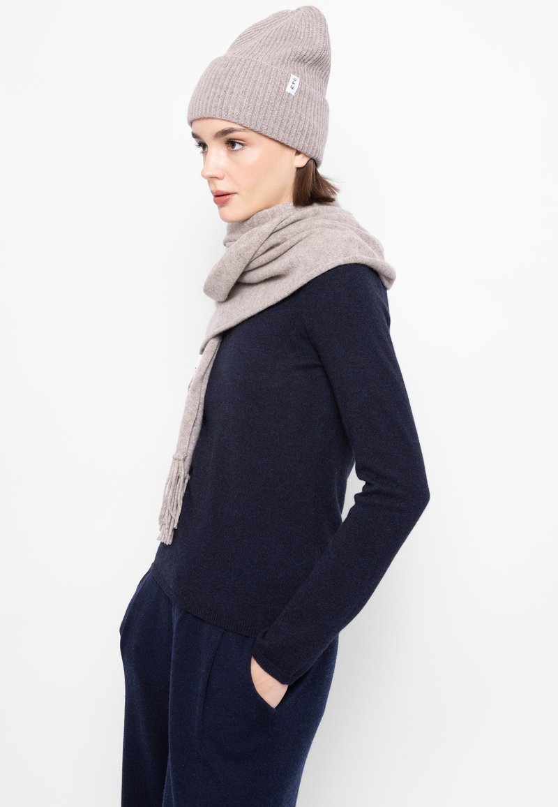 Világosszürke gyapjú sapka és hozzáillő sál egy sötétkék pulóveron, texturált anyagból készült, illeszkedő, lezser kialakítással.