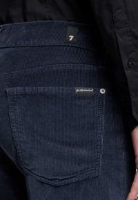 Pantaloni in velluto a coste blu navy con strisce verticali, dotati di tasca posteriore, etichetta cucita e dettaglio in metallo con bottone.