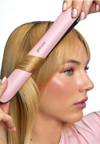 Ein pinkfarbener Haarglätter mit schwarzen Akzenten lockt eine Strähne glattes, blondes Haar und zeigt dabei sein elegantes Design und die glatte Textur.