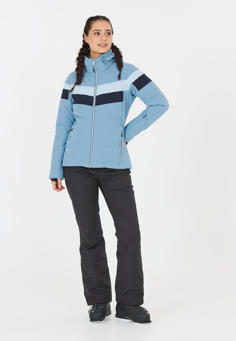 Himmelblå pufferjakke med marineblå og lys blå vandrette striber, fuld lynlås og to sidelommer. Kombination med sorte bukser og støvler.