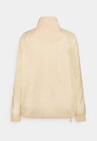 Giacca leggera di colore giallo chiaro, con collo alla coreana, polsini elasticizzati e orlo regolabile; texture liscia, design semplice e senza motivi visibili.