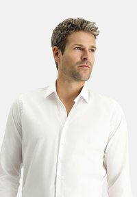 Camicia bianca con colletto standard, maniche lunghe e una texture liscia e senza pieghe. Vestibilità ben adattata e bottoni trasparenti.