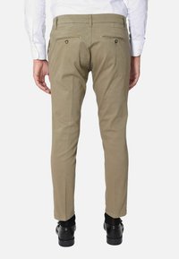 Chino khaki con vestibilità slim, dotati di tasche posteriori con chiusura a bottone, texture liscia e vita standard. Indossati con scarpe nere.