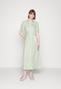 Vestido midi verde claro com padrão floral, colarinho, mangas curtas e fecho de botões na frente, combinado com sandálias.platformas lavanda.