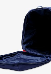 Bolso de tela azul marino con cierre de cremallera, que cuenta con un interior espacioso y un pequeño detalle rojo. El interior es oscuro y está forrado.