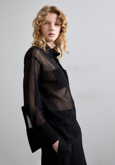 Transparante zwarte overhemd met lange mouwen, voorzien van een borstzak en gestructureerde manchetten, gestyled met gestructureerde zwarte broek.