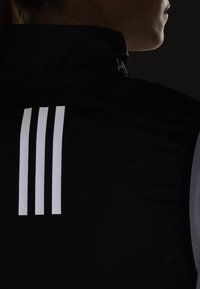 Czarna sportowa kamizelka z trzema pionowymi białymi paskami na plecach, o gładkiej fakturze i wysokim kołnierzu.