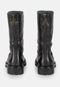 Botas de cuero negro hasta el tobillo con cremalleras dobles, acabado texturizado y suela de goma gruesa y moteada. Forro interior suave en un verde de contraste.