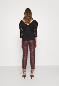 Mustat yläosa, jossa pitsiset puffihihat ja V-mallinen selkäosa, yhdistettynä burgundin värisiin nahkahousuihin ja mustiin nilkkureihin. Minimalistinen tausta.