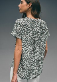 Leopardenmuster-Oberteil aus leichtem Stoff. Mit Rundhals, kurzen Ärmeln und abgerundetem Saum. Die Farben sind Grau und Schwarz.