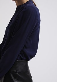 Blusa a maniche lunghe blu navy con scollo rotondo, tessuto morbido e vestibilità rilassata, abbinata a una gonna aderente in pelle nera.