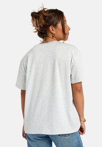 Camiseta gris de manga corta hecha de tejido suave, con un corte holgado y cuello redondo, mostrada desde la parte de atrás con costuras visibles.