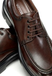 Braune Leder-Desserschuhe mit abgerundeter Zehenpartie, sechs Ösen und dunklen Schnürsenkeln. Strukturierte Oberfläche und erhabene Nähte entlang der Kanten.