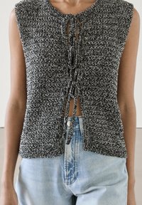 Czarny i biały, fakturowany top bez rękawów z okrągłym dekoltem i regulowanym wiązaniem z koronką z przodu, w połączeniu z jasnoniebieskimi dżinsami.