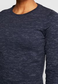 Navy blue long-sleeve knit top with a textured, speckled pattern and a classic crew neckline. Material appears soft and stretchy.