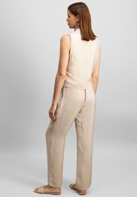 Beige ärmelloses Oberteil mit Kragen, kombiniert mit passenden hellen Hosen. Weicher, strukturierten Stoff, lockere Passform und dezente Designdetails.