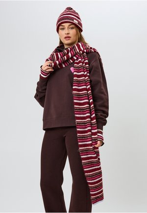 Barna pulóver rózsaszín és fehér csíkos részletekkel, hozzáillő csíkos sál bordó és szürke színekben, valamint csíkos sapka bojtos díszítéssel.