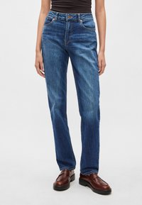 Mėlynos spalvos džinsai iš džinso medžiagos su aukštu liemeniu, tiesiomis kojomis ir subtiliais pageltimus primenančiais raštais. Komplekte yra priekinės ir galinės kišenės, metalinis užsegimas ir kontrastingos siūlės.