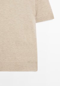 Maglione beige a maniche corte, con scollatura a girocollo, posato su uno sfondo bianco, che mette in evidenza una texture morbida.