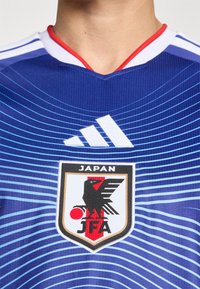 Närbild av en blå japansk fotbollsjersey med Japan Football Association-logotypen och Adidas-emblemet på bröstet.