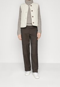 Prošívaná krémová vesta na knoflíky, doplněná šedým rolákem a tmavě hnědými kalhotami s širokými nohavicemi. Outfit doplňují bílé tenisky.