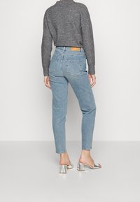 Jeans azzurri chiari con vita alta e leggermente svasati, realizzati in denim. Abbinati a un maglione grigio a maglia e sandali con tacco blocco argentati.