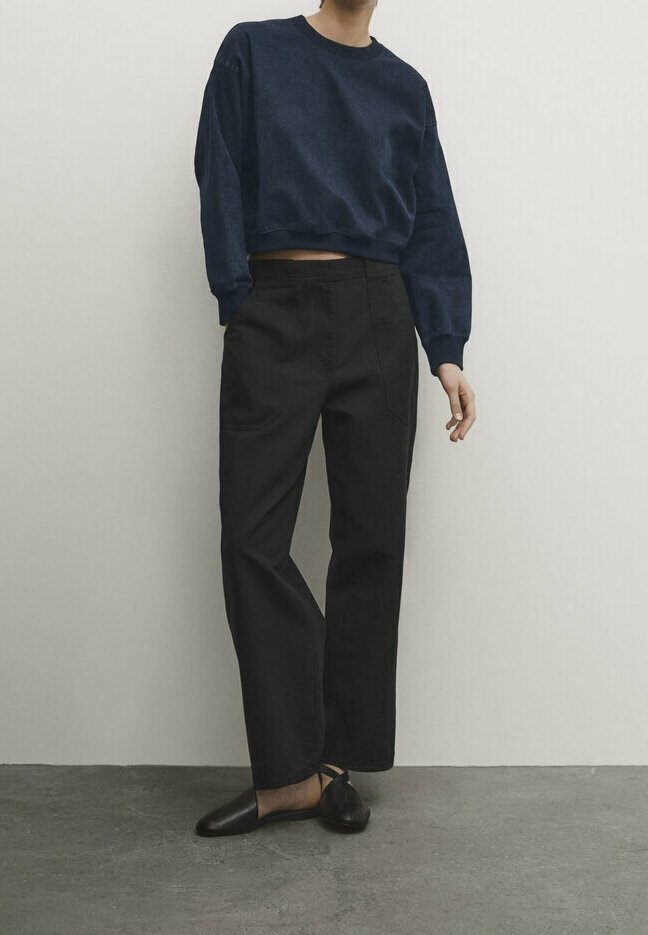 Laivastonsininen lyhyt collegepaita yhdistettynä korkeavyötäröisiin mustiin housuihin. Kengät ovat mustat, liukusäädettävä malli, jossa on terävä kärki. Sileä kangaspinta.