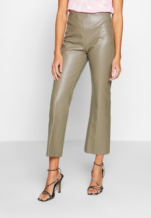 Donna che indossa pantaloni cropped in pelle verde oliva a vita alta e sandali neri con tacco alto e cinturini alla caviglia.