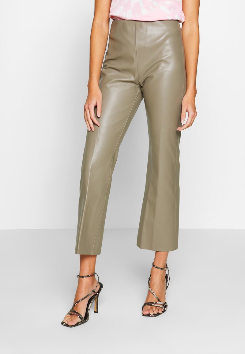 Kvinna som bär högmidjade olivgröna läderbyxor i cropped-modell och svarta, strappy högklackade sandaler med ankelsnören.